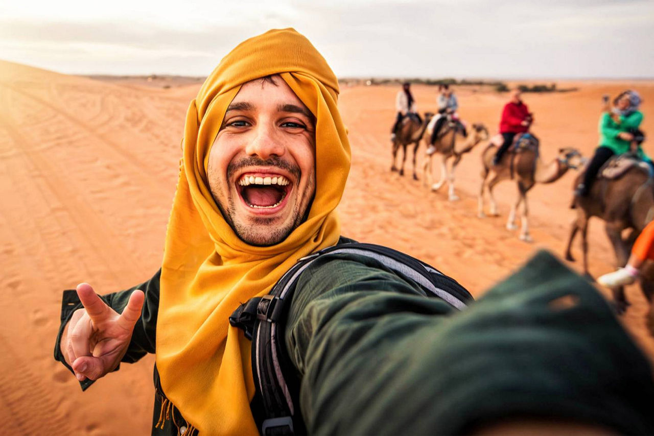 Junger Mann macht in der Wüste auf einem Kamel ein Selfie
