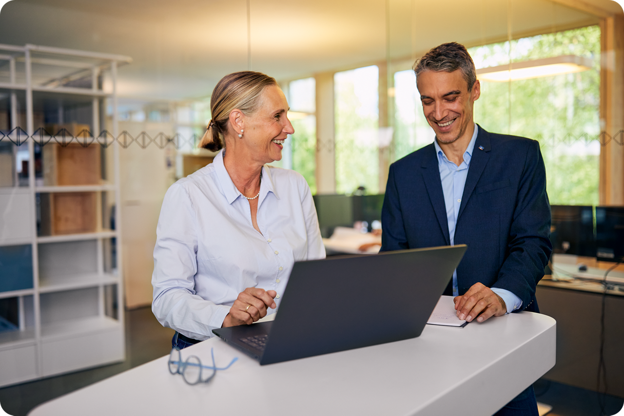 Eine Frau und ein Mann stehen am Tisch und schauen gemeinsam auf ein Notebook