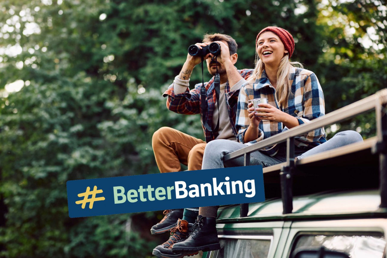 junges glückliches Paar sitzt auf Dach eines Campers, der Mann schaut durch ein Fernglas