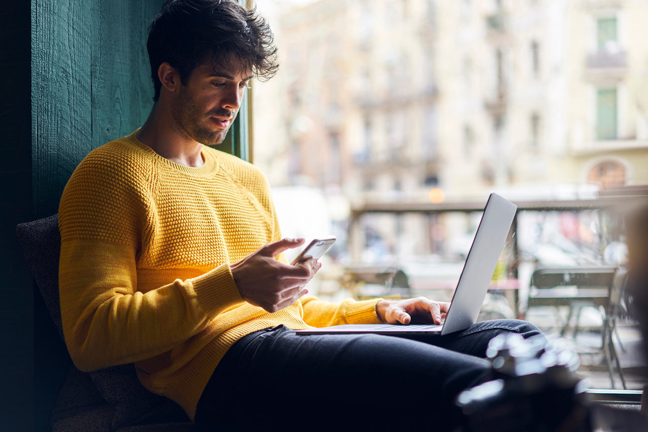 Ein Mann sitzt bequem vor einem Fenster mit seinem Handy in der Hand
