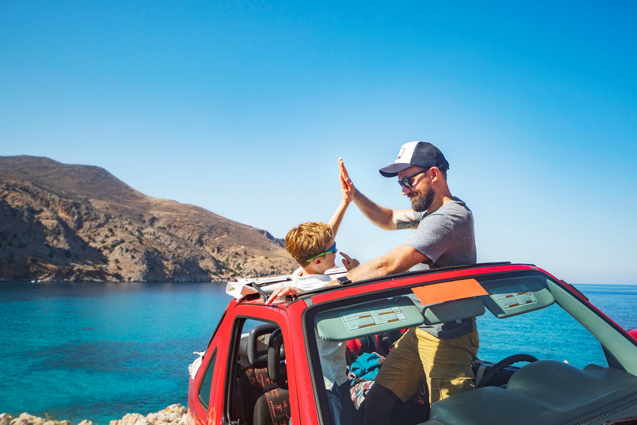 Vater und Sohn sitzen im Auto am Strand und geben sich einen highfive