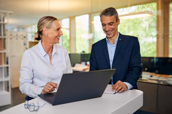 Frau und Mann stehen lachend vor einem Laptop