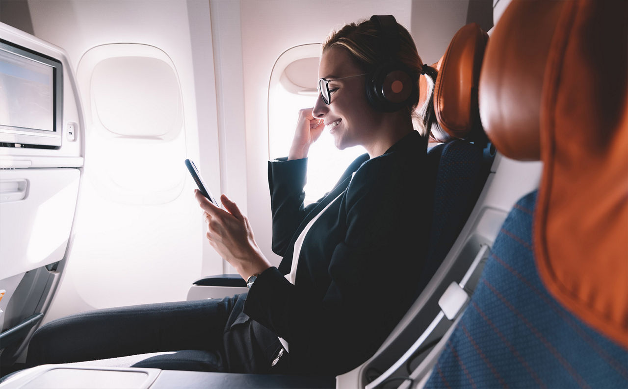 Junge Frau blickt im Flugzeug auf ihr Handy