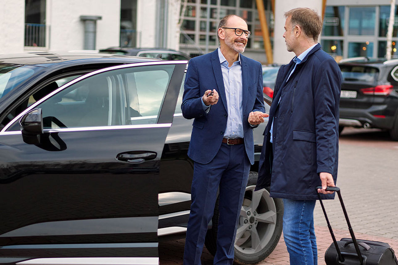 Zwei Männr im Anzug vor einem schwarzen Auto