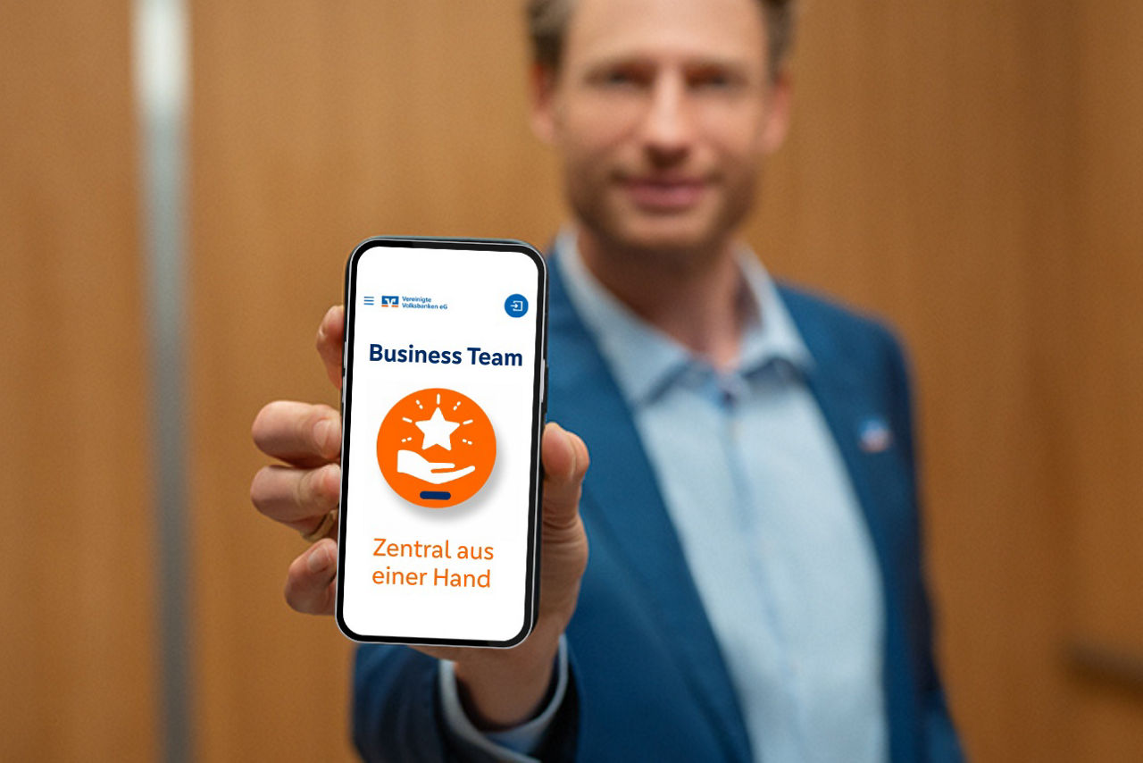 Mann (Berater) zeigt Smartphone-Bildschirn im die Kamera. Zu lesen ist: "Business Team – Zentral aus einer Hand."