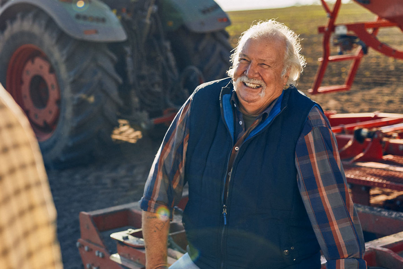 Älterer Mann sitzt lachend auf einer Landmaschine