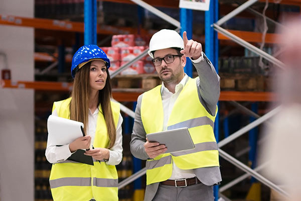 Mann und Frau mit Helm und Warnwesten in einer Lagerhalle