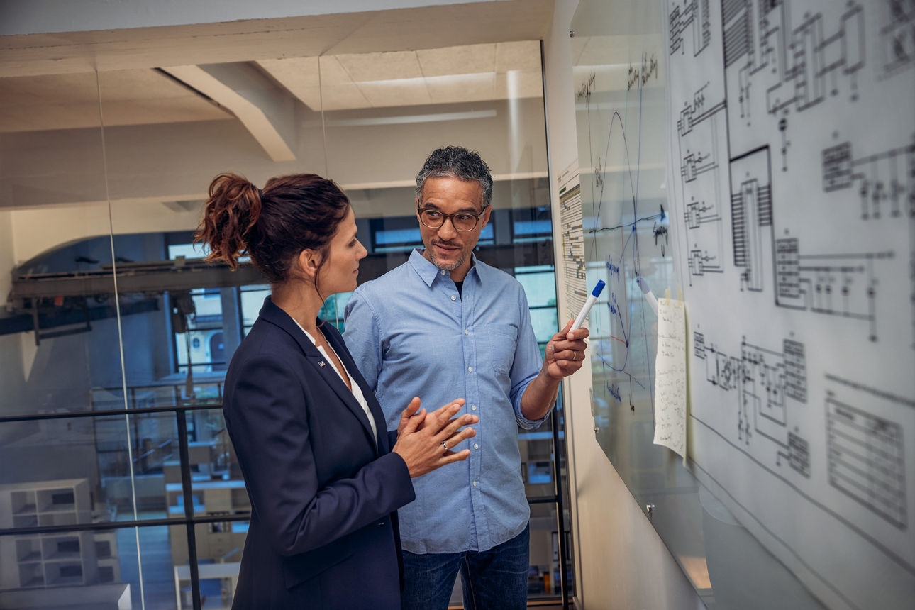 Beraterin und Geschäftsführer arbeiten im Büro an einem Whiteboard.