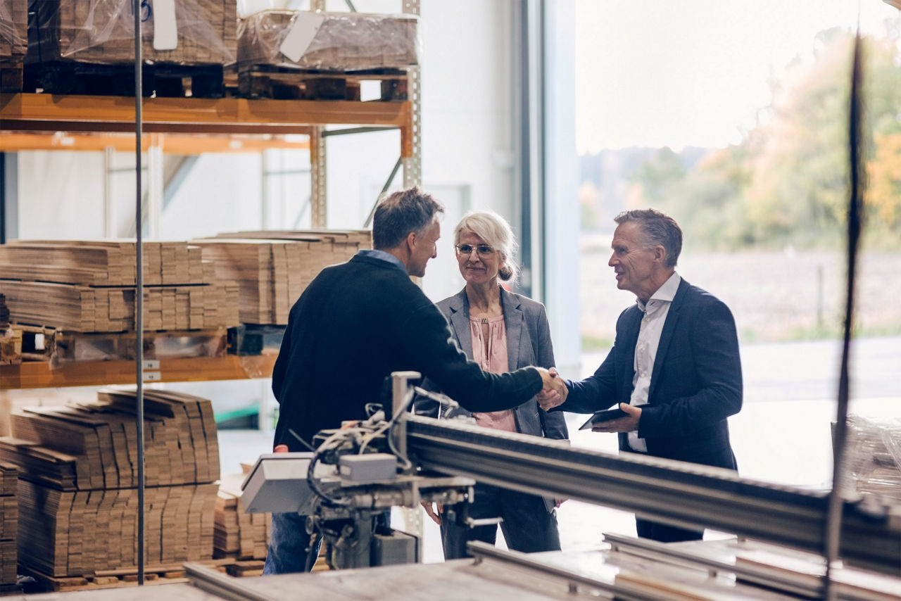Zwei Männer und eine Frau begrüßen sich in einer Produktionshalle.