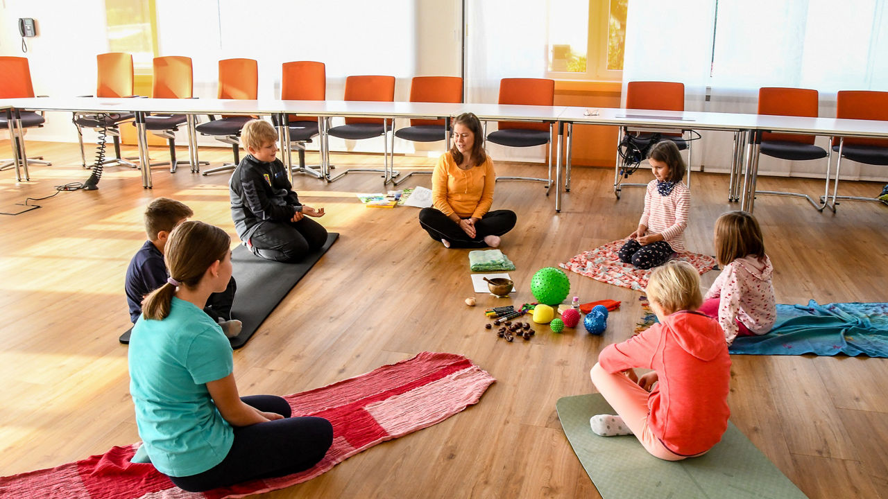 Die Teilnehmenden sitzen auf ihren Yoga-Matten im Kreis und schauen die Lehrerin an