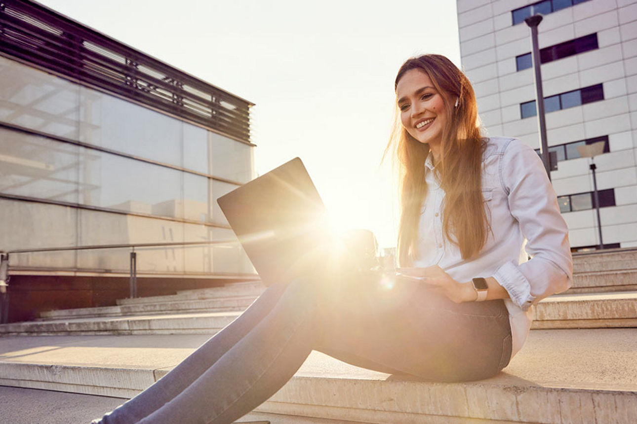 Junges Mädchen sitzt mit dem Laptop auf den Stufen beim Sonnenuntergang.