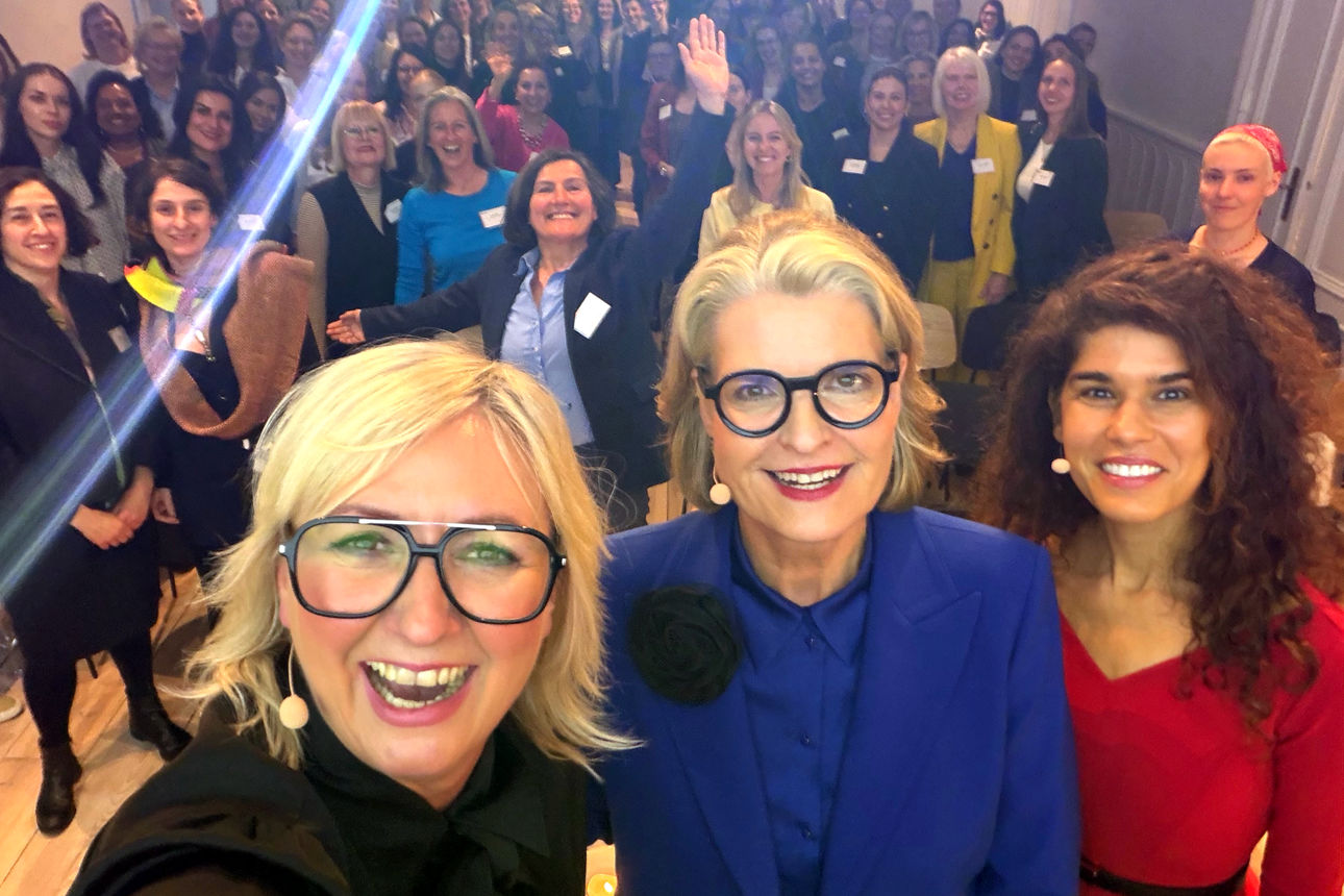 Gruppen-Selfie bei einer Veranstaltung mit drei Personen vor einem großen Publikum.