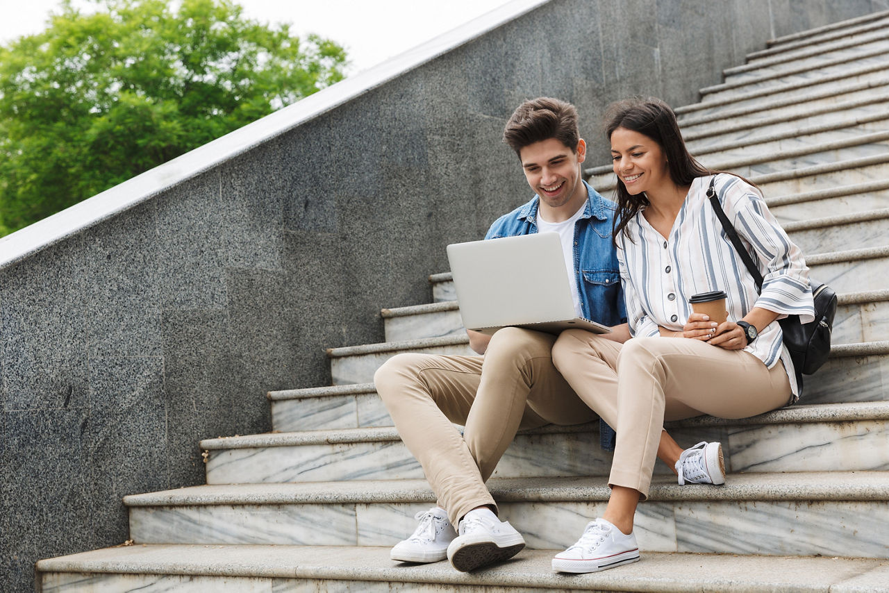 Ein Student und eine Studentin sitzen auf einer Treppe und schauen auf einen Laptop