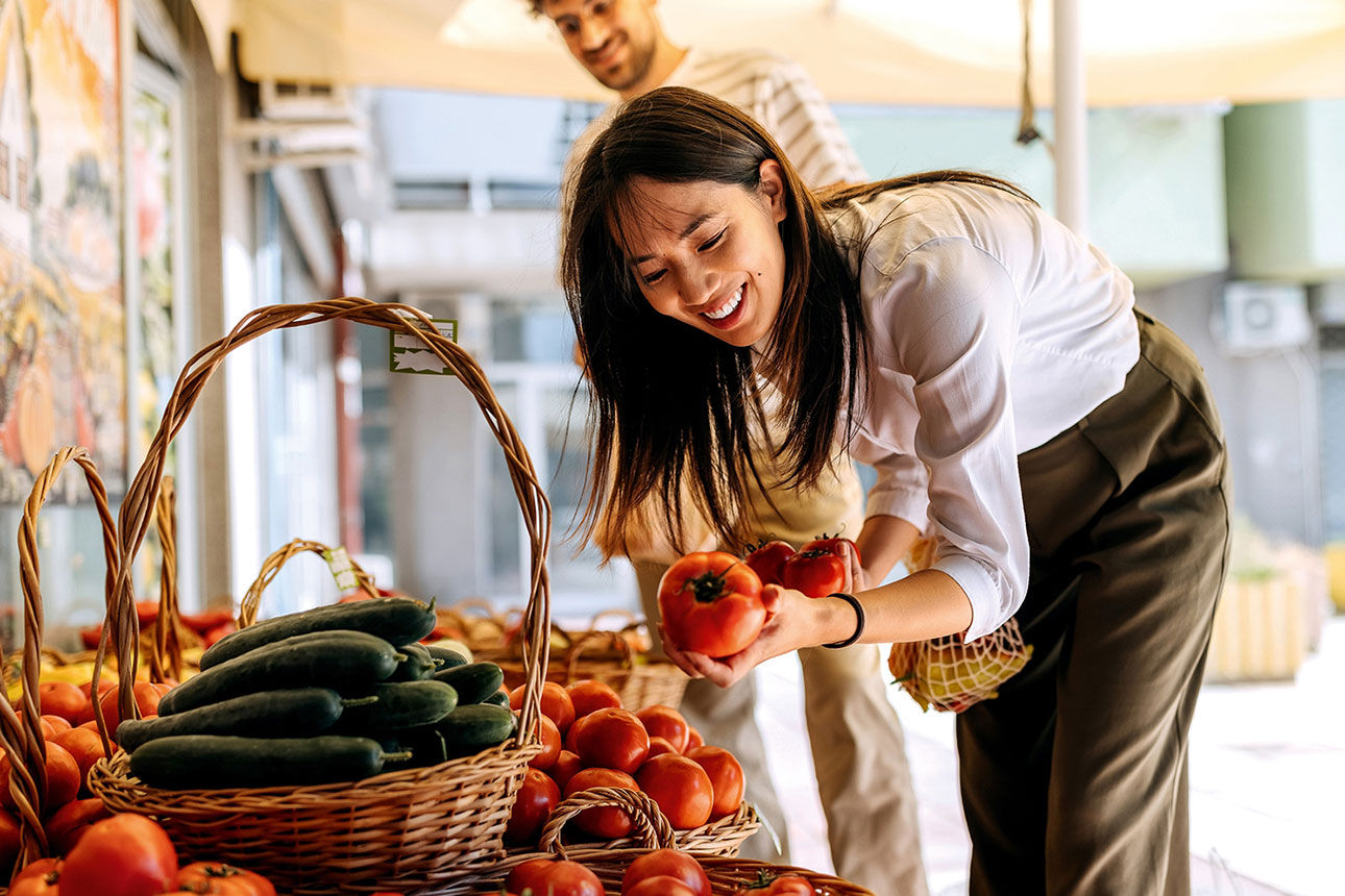 Frau steht vor einem Obst und Gemüse regal 