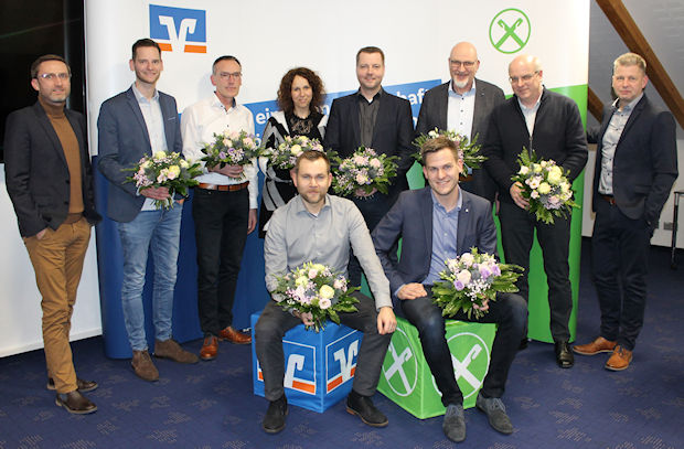Eine Gruppe von neun Männern und einer Frau steht vor einem Banner mit den Logos von zwei Unternehmen.
