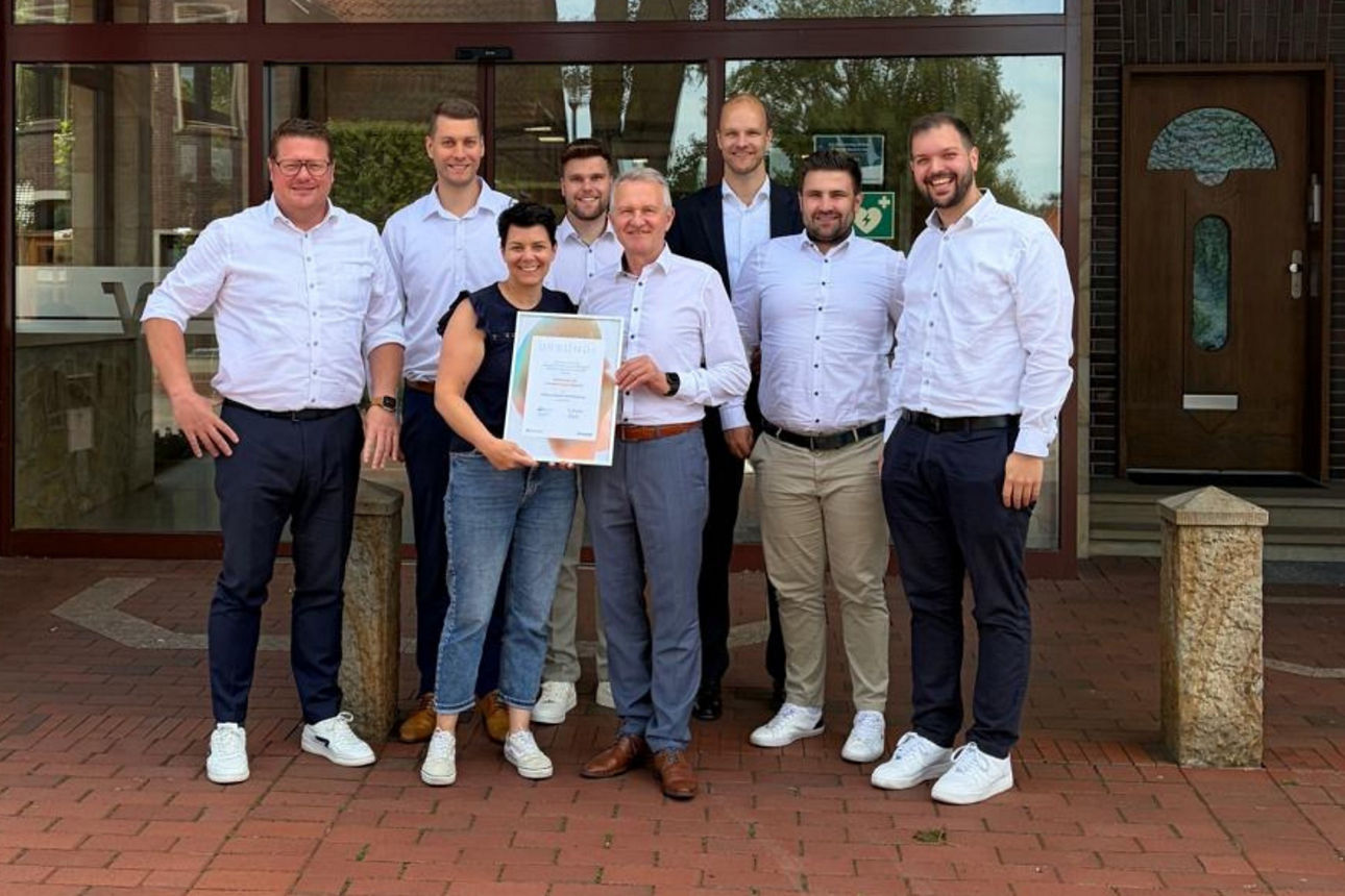 Ein Gruppenfoto, auf dem eine Frau und ein Mann eine gerahmte Urkunde in der Hand halten.