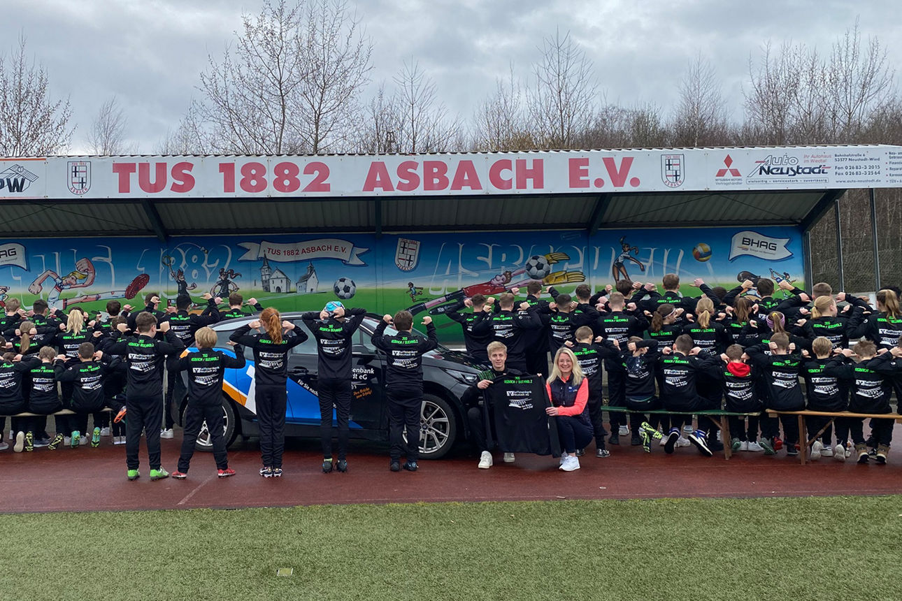 Jugendliche des TuS Asbach stehen in einer  Reihe und zeigen auf die Logos auf ihren Trikotrücken