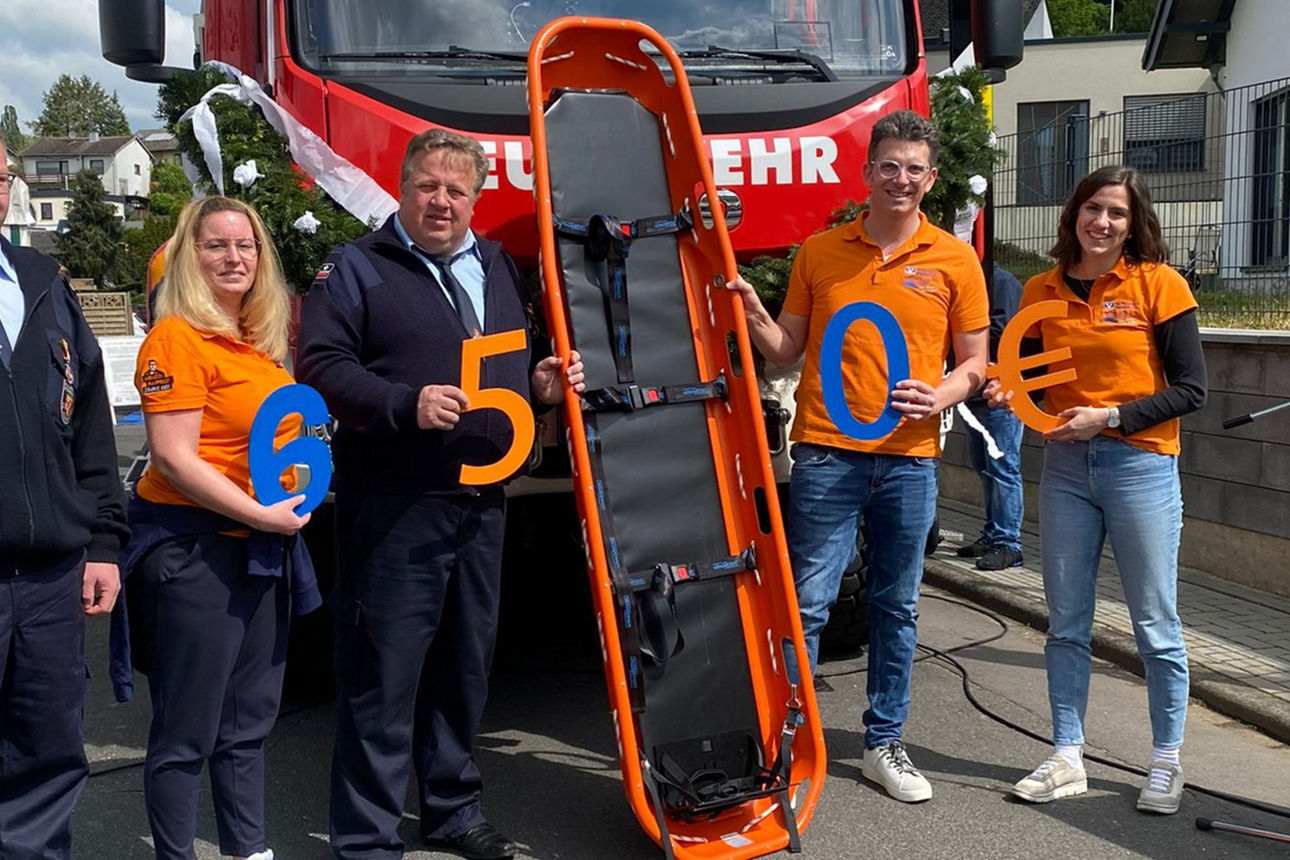 Mitglieder der Feuerwehr Straßenhaus-Oberraden und Mitarbeitende der Raiffeisenbank mit Korbtrage vor einem Feuerwehrauto