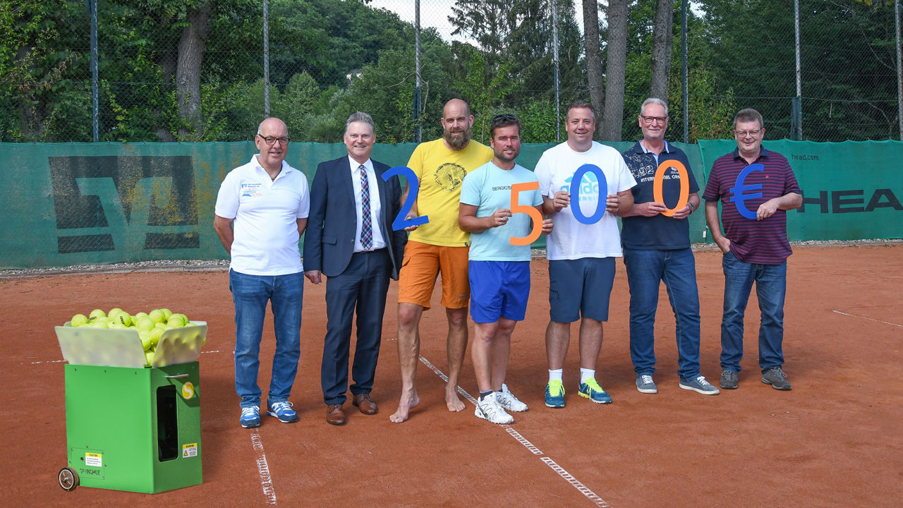 Mitarbeitende der Raiffeisenbank stehen mit Mitgliedern des Tennisbereichs neben der neuen Ballmaschine auf dem Tennisplatz
