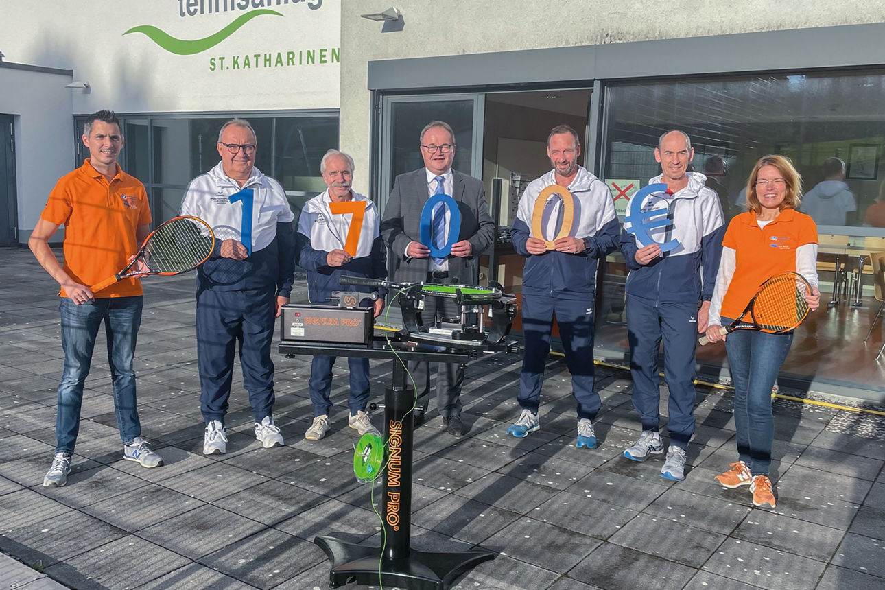 Mitglieder des TC St. Katharinen und Mitarbeitende der Raiffeisenbank stehen um eine Besaitungsmaschine für Tennisschläger
