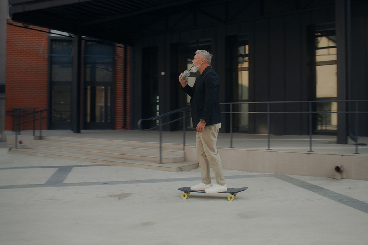 Mann fährt auf einem Skateboard und trinkt einen Smoothie