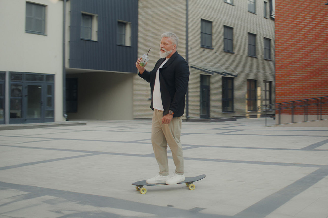Mann fährt auf einem Skateboard und hat einen Smoothie in der Hand.