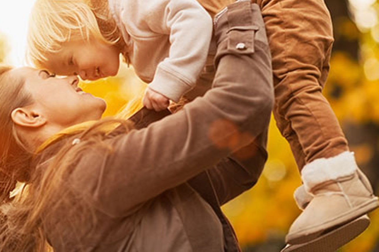 Mutter hält ihr Kind hoch an einem sonnigen Herbsttag