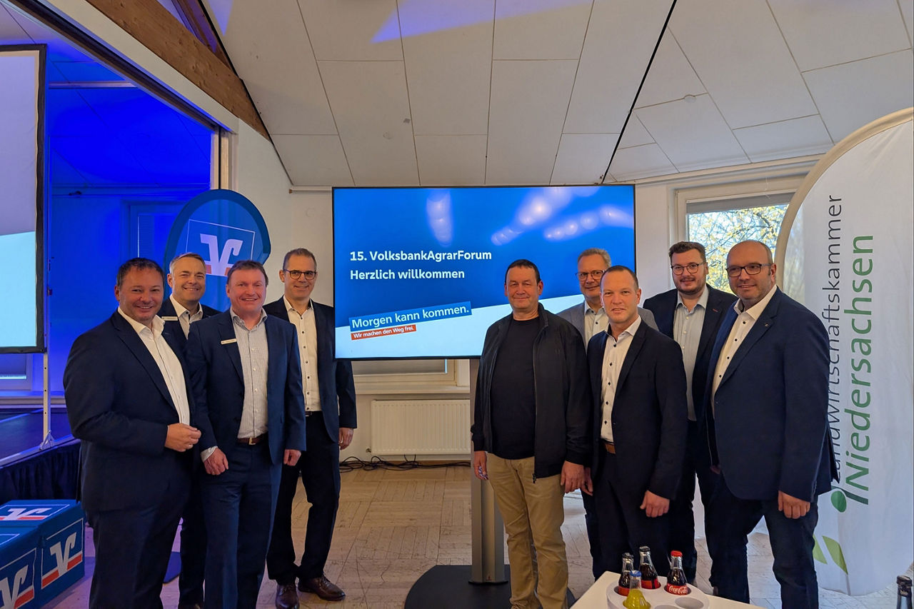 Neun Personen in Businesskleidung vor einer Leinwand mit einer Präsentationsfolie