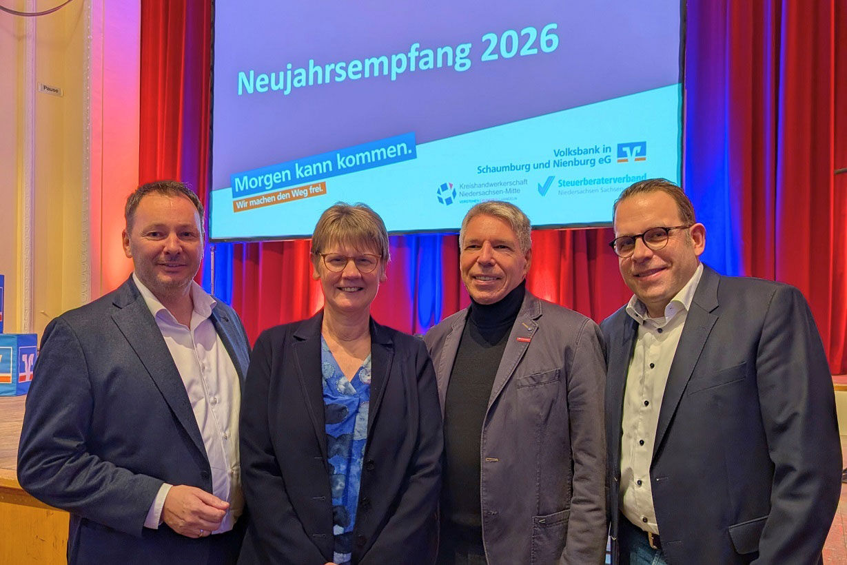 Vier Personen in Businesskleidung vor einer Leinwand mit einer Präsentationsfolie, auf der "Neujahrsempfang 2026" steht