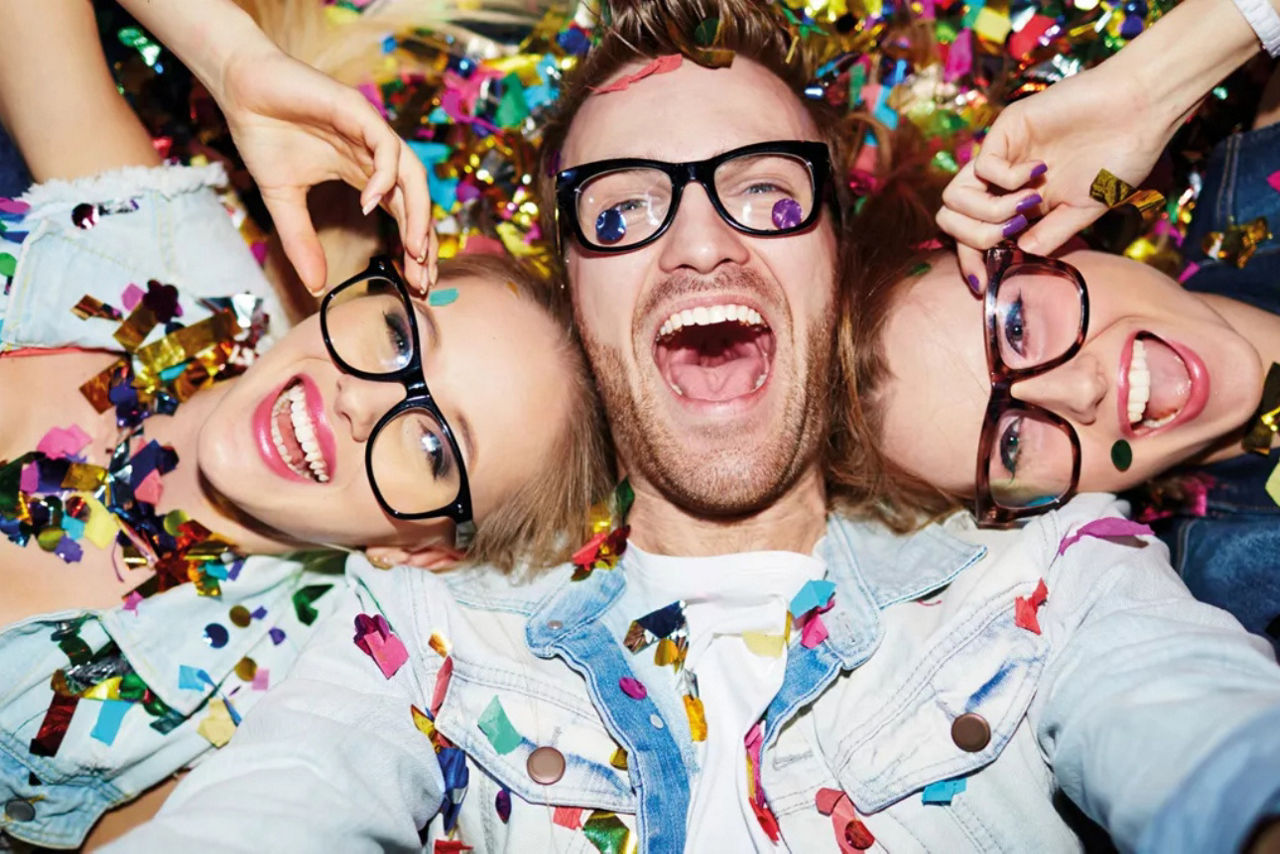 Drei Schulabgänger mit Brille sind bedeckt mit Konfetti und liegen lachend auf dem Rücken.
