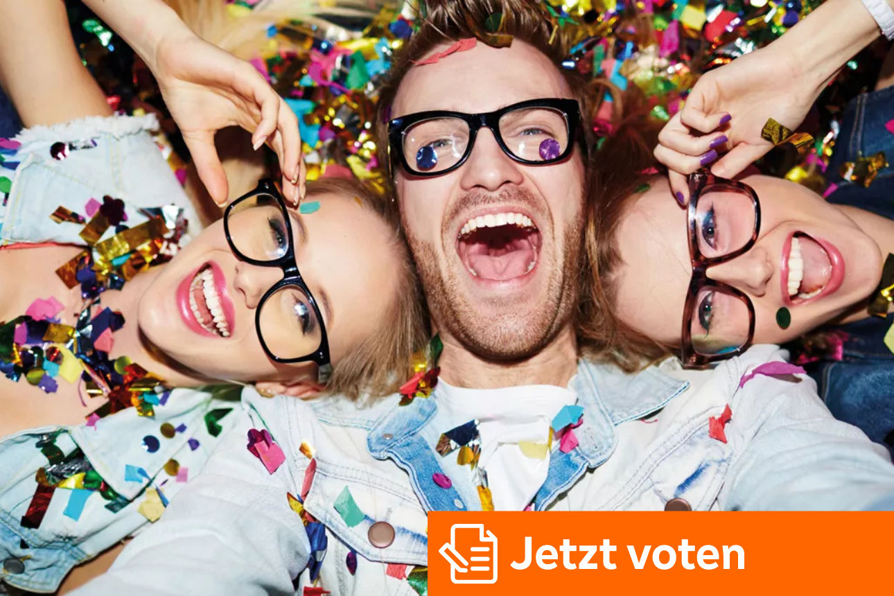 Drei Schulabgänger mit Brille sind bedeckt mit Konfetti und liegen lachend auf dem Rücken.