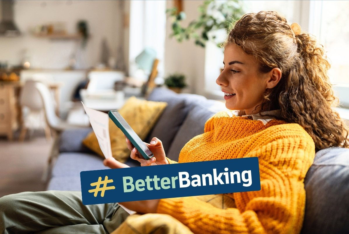 Junge Frau sitzt mit Smartphone und Rechnung in den Händen auf dem Sofa