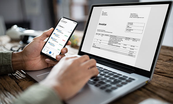 Mann hat auf dem Laptop eine Rechnung und schaut parallel auf seine Banking App
