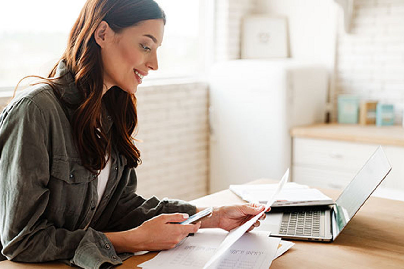 Frau mit Laptop am Schreibtisch prüft eine Rechnung