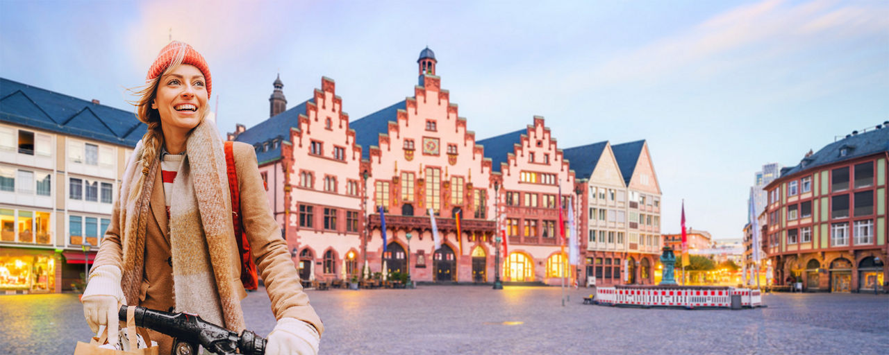 Ein junge blonde Frau auf einem E-Scooter und im Hintergrund der Römer-Platz in Frankfurt am Main.