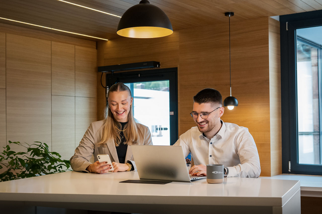 Zwei Personen sitzen an einem Schreibtisch und arbeiten an einem Laptop