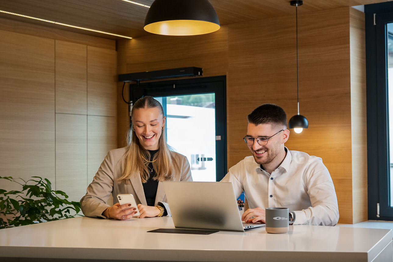 Zwei Personen sitzen an einem Schreibtisch und arbeiten an einem Laptop