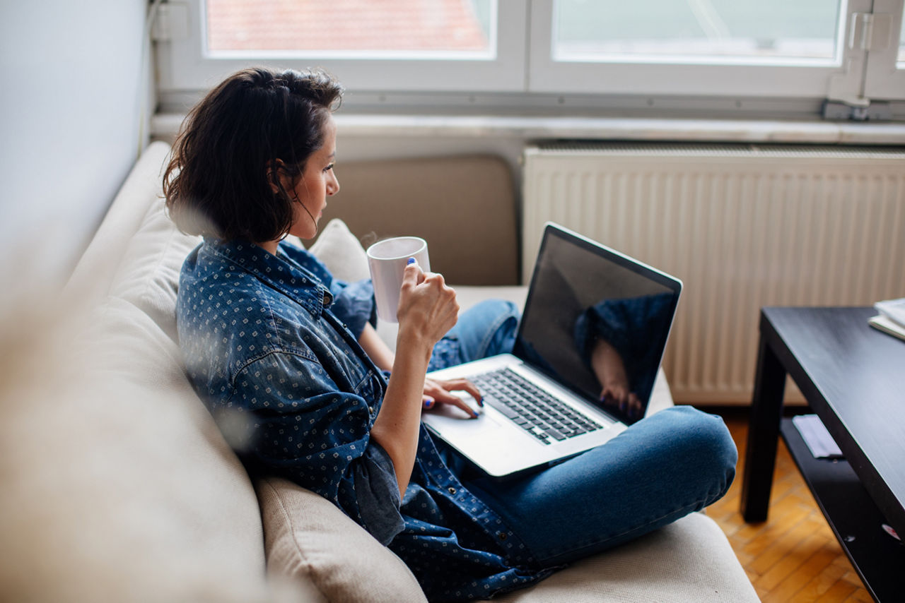 Eine Frau ist an Ihrem Laptop und trinkt einen Kaffee