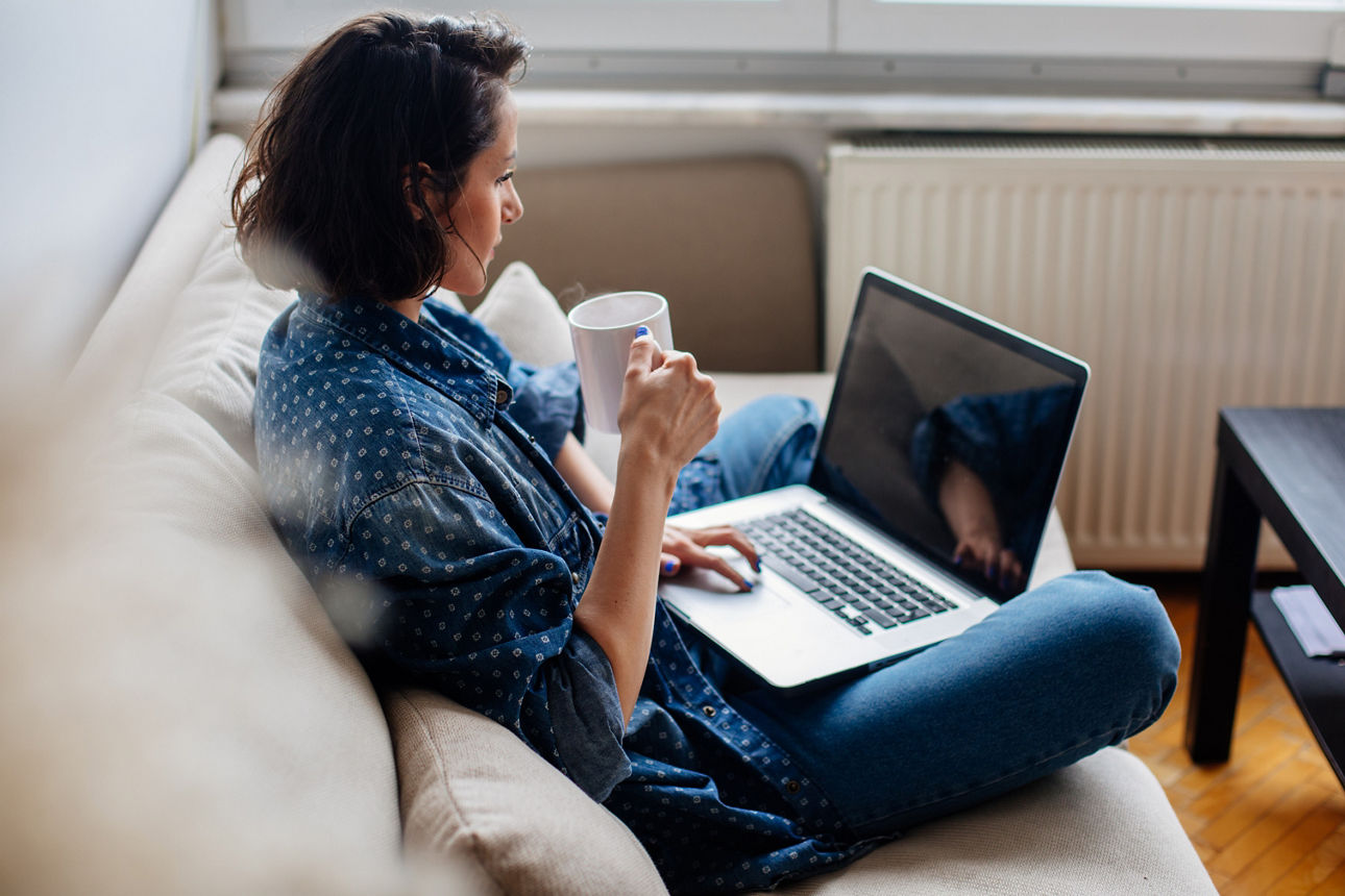 Eine Frau ist an Ihrem Laptop und trinkt einen Kaffee
