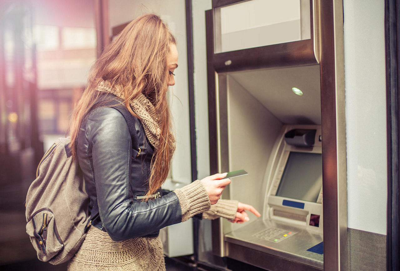 Eine junge Frau will ihre Bankkarte in den Geldautomaten stecken, um Geld abzuheben.