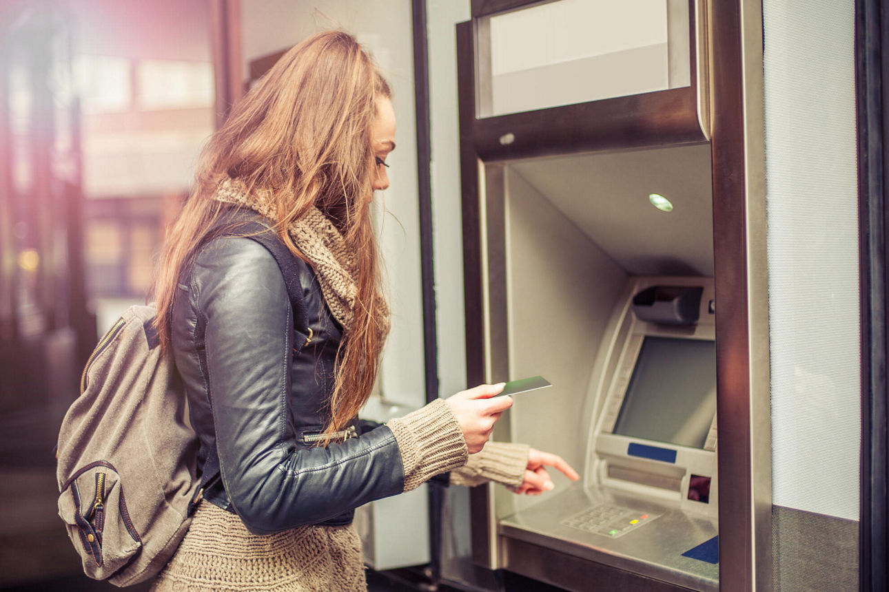 Eine junge Frau will ihre Bankkarte in den Geldautomaten stecken, um Geld abzuheben.