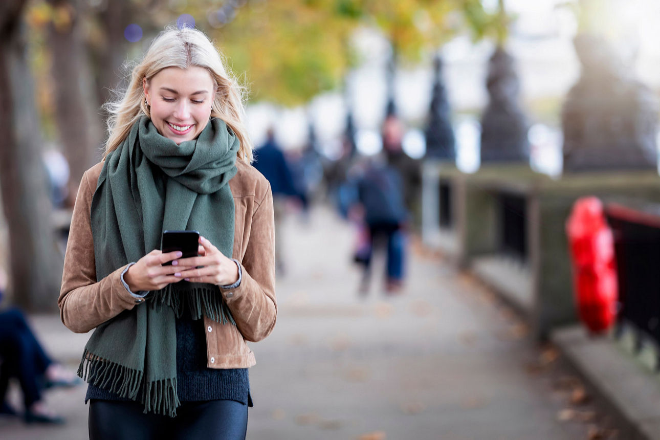 Blonde Frau läuft draussen im Herbst mit Mobiltelefon