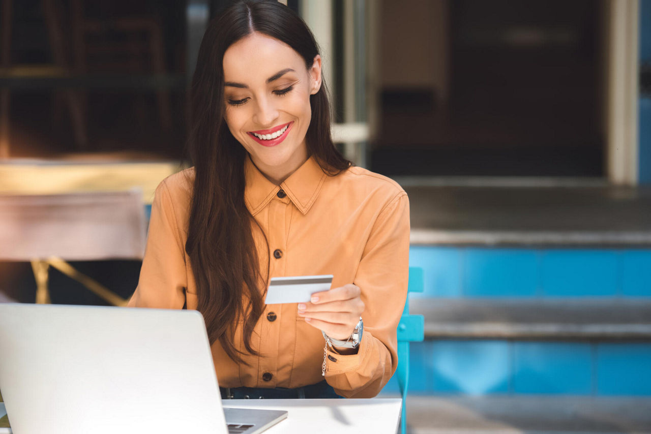 Eine Frau sitzt am Laptop und hält eine BusinessCard in der Hand