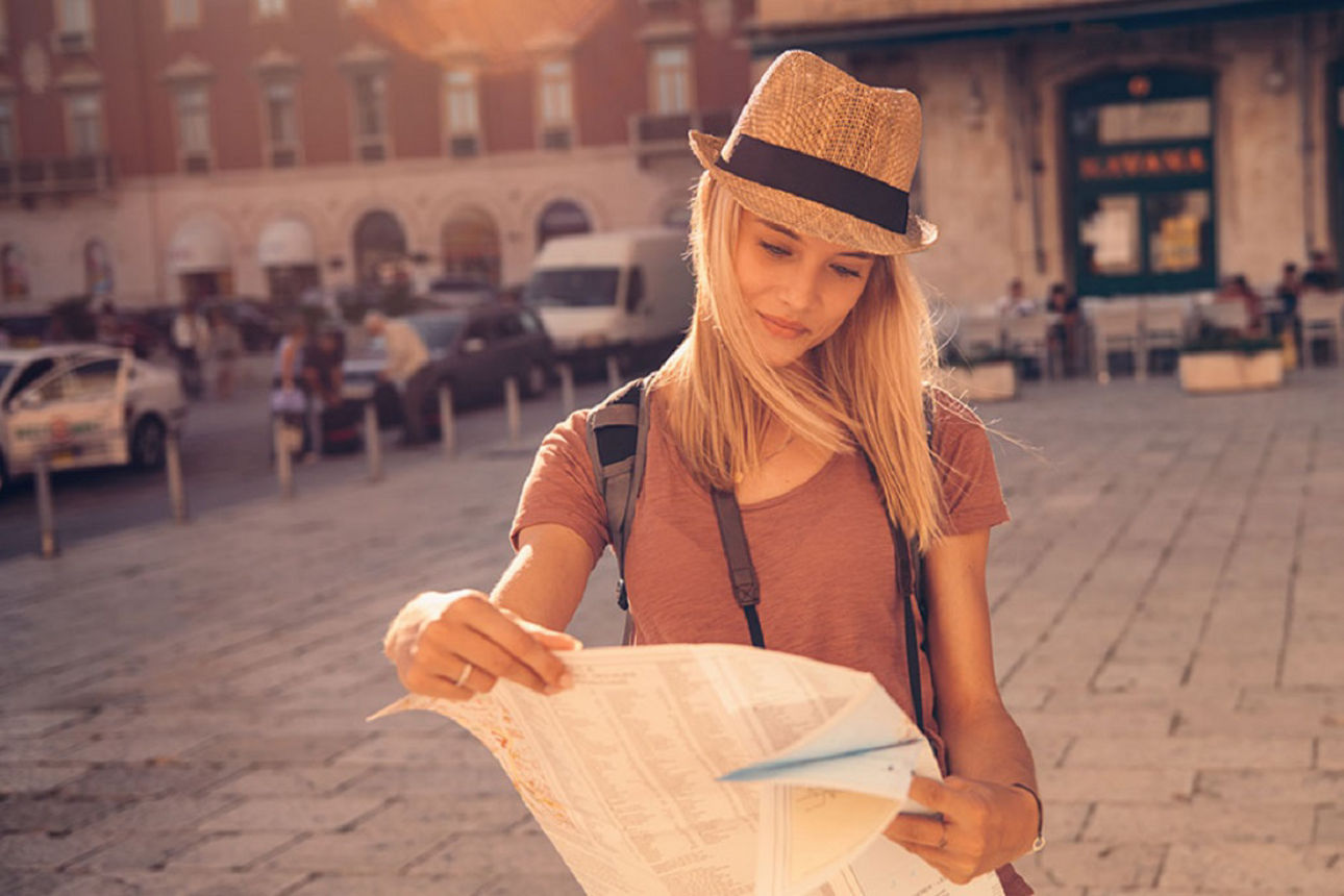 Frau mit Sommerhut steht auf Marktplatz und erkundet die Stadtkarte