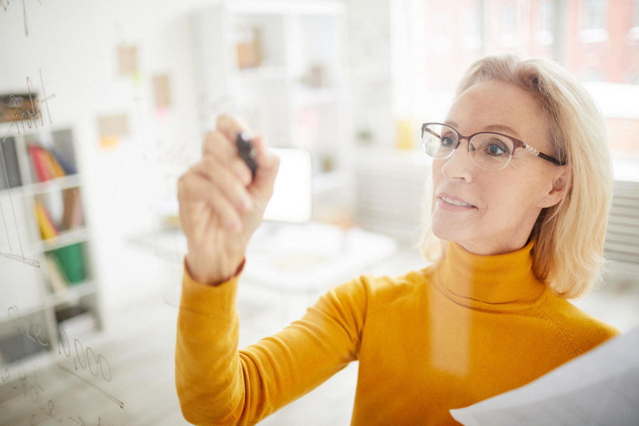 Eine blonde Frau die auf ein Whiteboard schreibt.