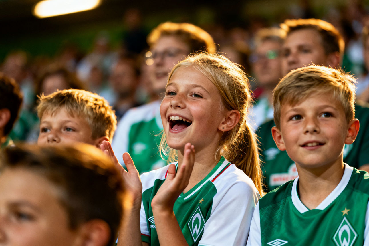 Mehere Kinder im Werder Bremen Trikot sitzend im Stadion