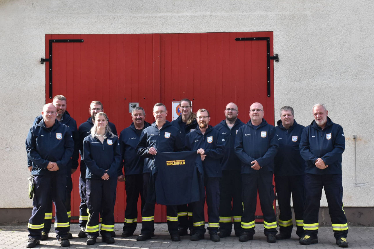 Mitglieder der Freiwilligen Feuerwehr Kuhlenfeld stehen mit ihren neuen Softshelljacken vor dem Feuerwehrgebäude
