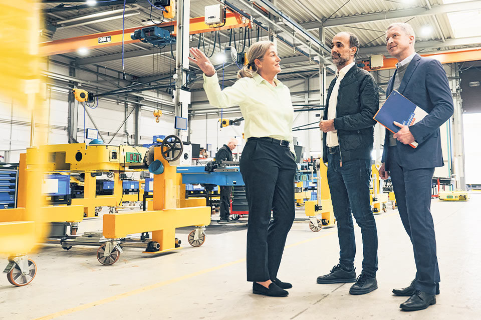 Drei Personen stehen in einer Produktionshalle und diskutieren