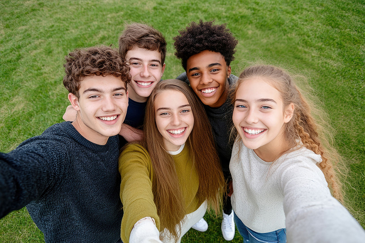 Fünf Jugendliche, drei Mädchen und zwei Jungen, sitzen draußen auf einer Bank, lachen und reden.