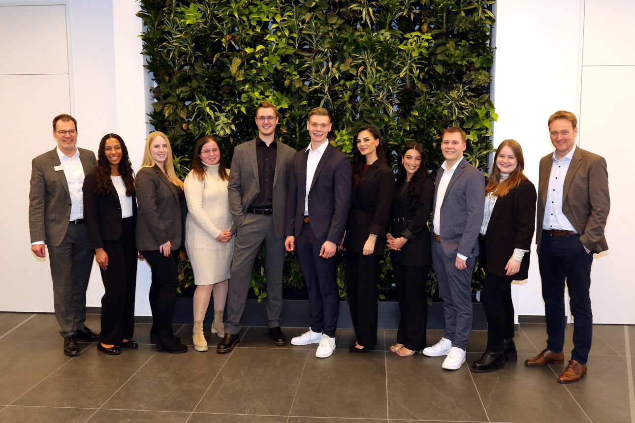 Eine Gruppe von Absolventen die vor einer Pflanzenwand stehen. 